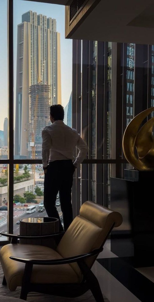 Executivo diante da janela de um edifício corporativo, observando a cidade.